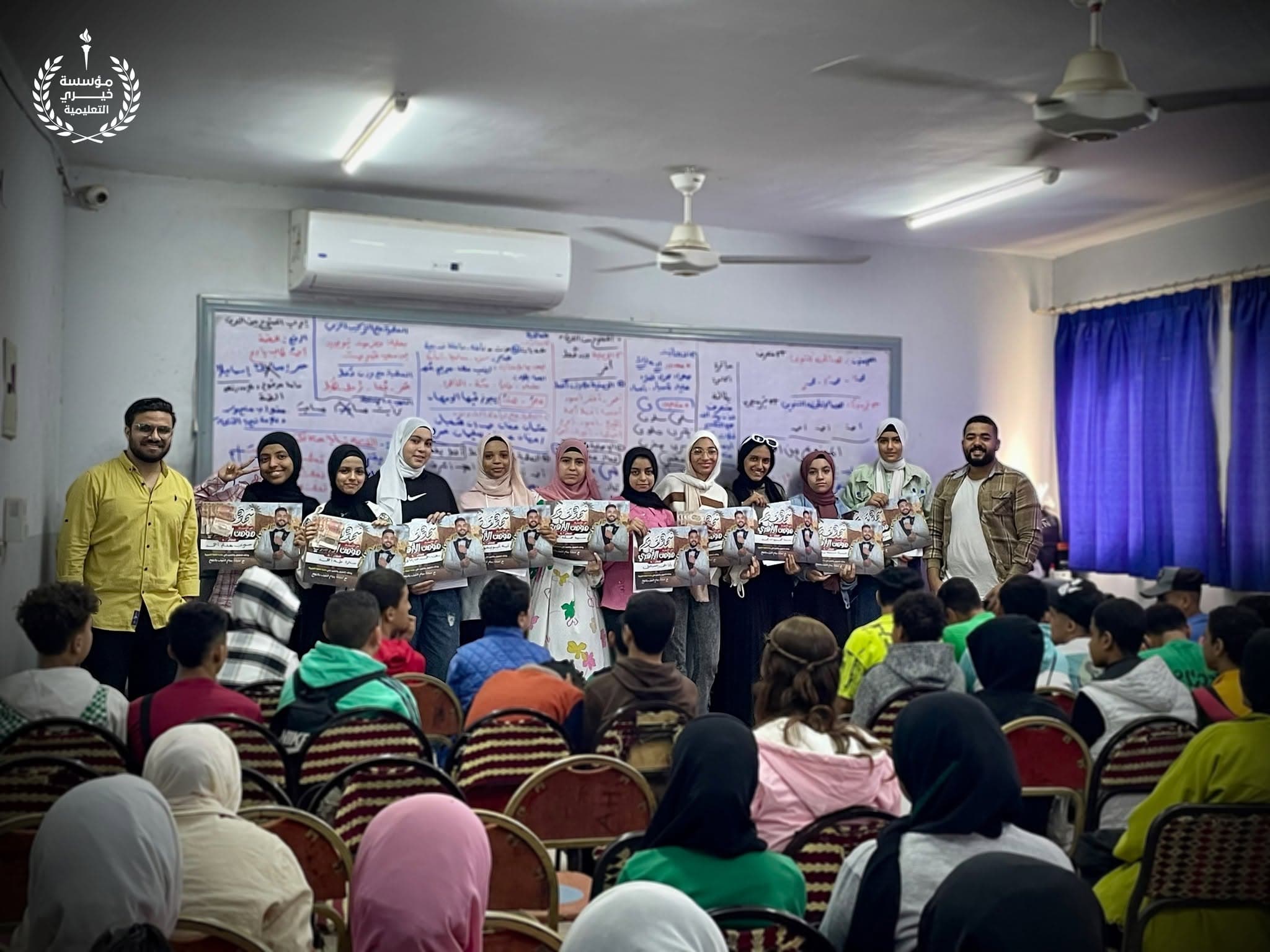طالبات يحملن ملصقات تكريم أمام قاعة ممتلئة بالحضور