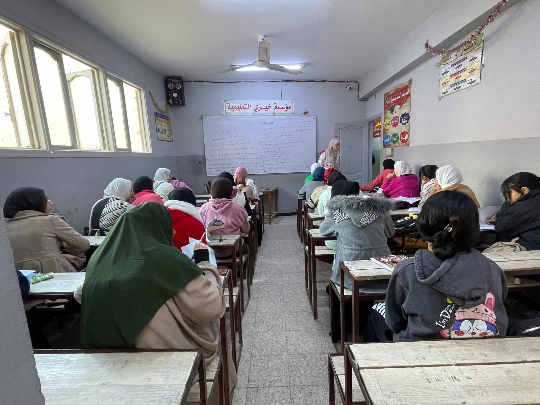مدرّسة تشرح درس لغة إنجليزية على السبورة أمام طلاب الفصل