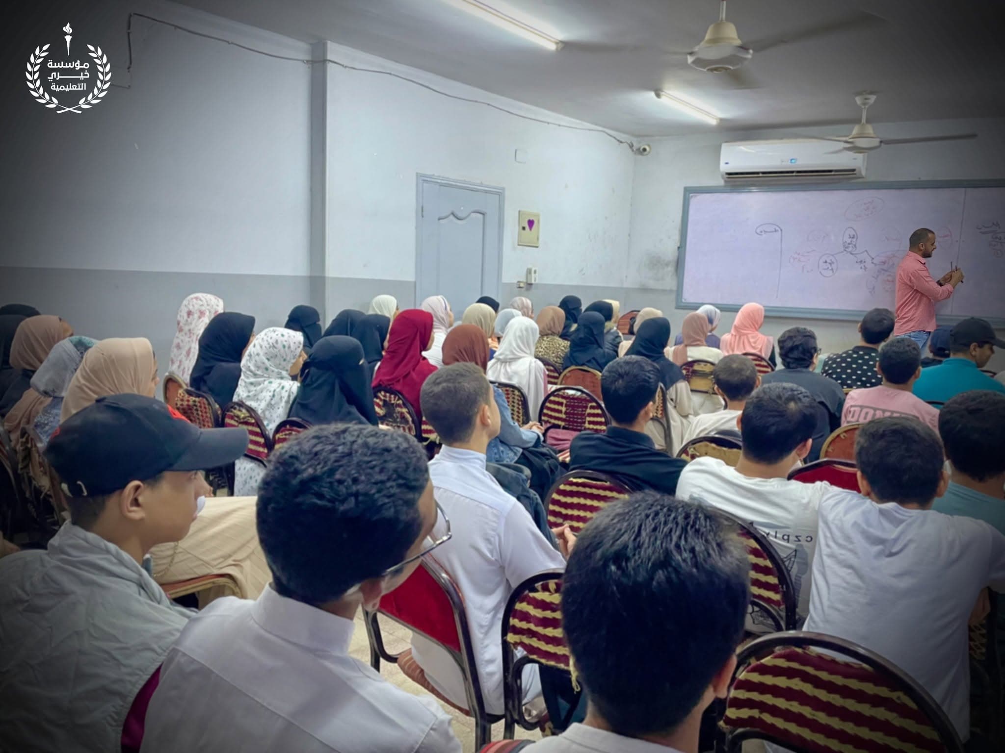 طلاب وطالبات يتابعون شرح المدرّس داخل إحدى قاعات المؤسسة