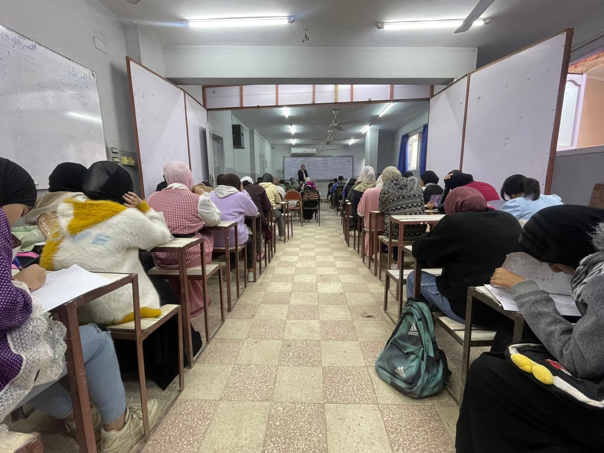 طلاب يؤدون امتحانًا على صفوف من المقاعد داخل قاعة طويلة