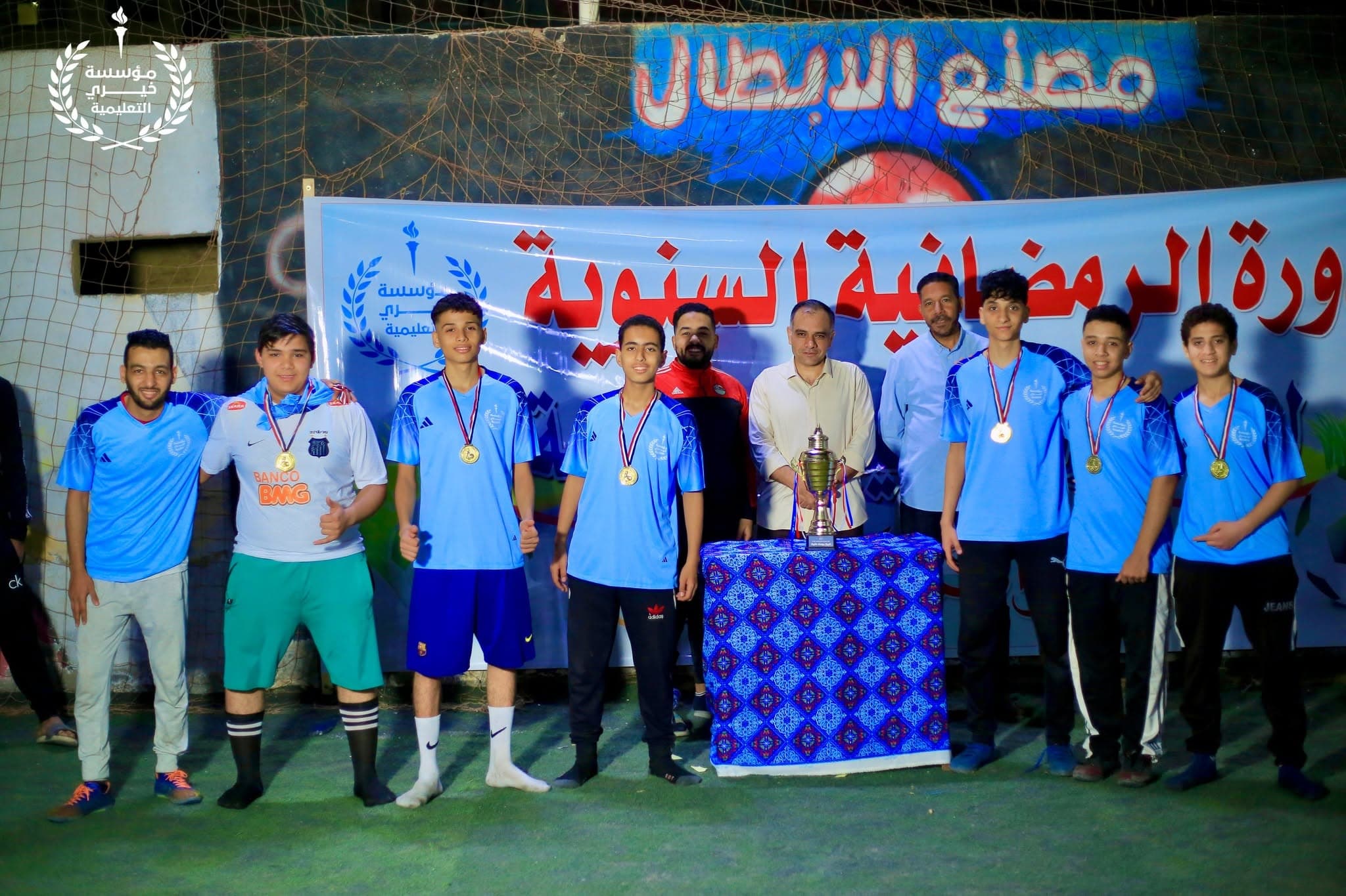فريق الطلاب بالميداليات مع المشرفين أمام لافتة الدورة الرمضانية السنوية